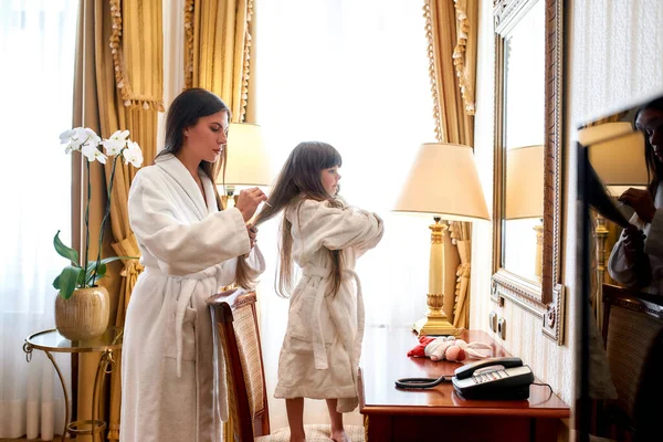 Бережи себе. Кавказька мати й дочка відпочивають у затишному готельному номері. Мама чистить холодне волосся. Поняття сім'ї, любові, турботи — стокове фото