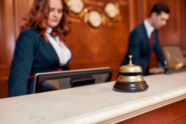 We always hear you. Attractive executives at the reception desk of a hotel in the background. Focus on a service bell