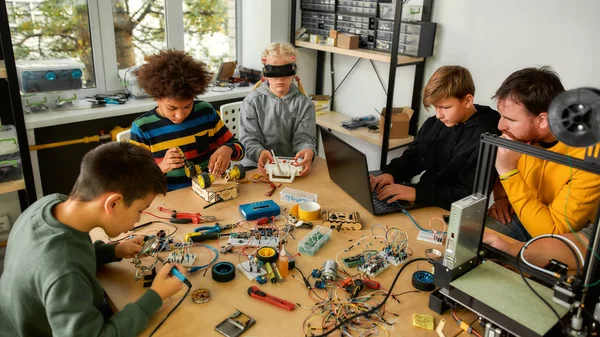 Teamwork. Young technicians building robots and vehicles, using soldering iron to join chips and wires, testing and programming toys together with a male teacher at a stem robotics class — Stock Photo, Image