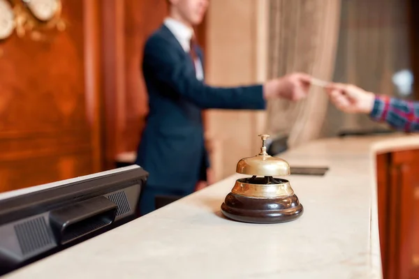 Always hear you. Young executive at the reception desk of a hotel working in the background. Focus on a service bell — Stock Photo, Image