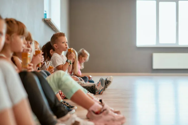 Rimanere idratato. Gruppo di bambini carini e positivi seduti sul pavimento nella sala da ballo e bere succo di frutta. Rilassante dopo il corso di coreografia — Foto Stock