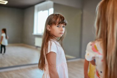 Dans stüdyosunda aynaya bakarken kameraya bakan küçük tatlı bir kızın portresi. Koreografi dersi alan bir grup çocuk.