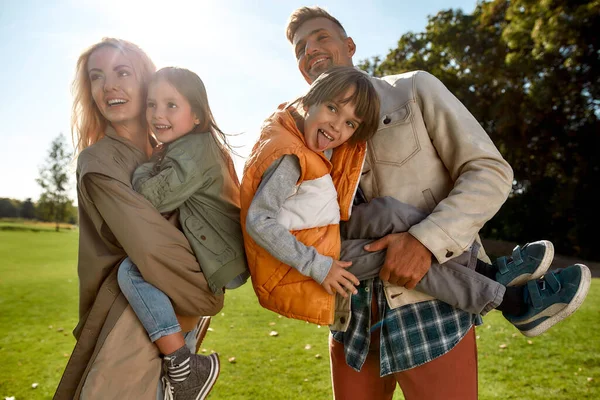 Familia positiva y feliz. Los padres jóvenes y sus hijos están disfrutando de un día soleado y divirtiéndose juntos mientras están de pie en un prado verde —  Fotos de Stock