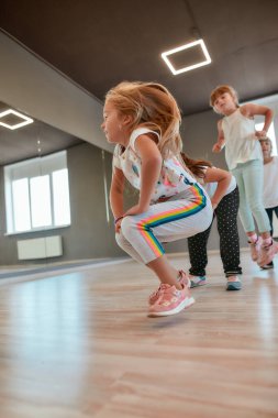 Dynamic warm up. Little active boys and girls in casual clothes warming up in the dance studio. Children doing sport exercises