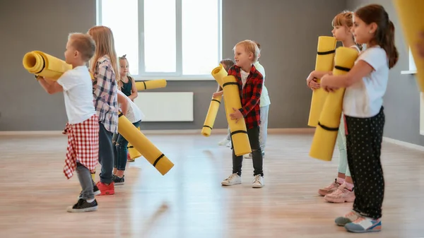 Doing yoga after training. Group of cute little boys and girls in casual clothes holding yoga mats while standing in the dance studio — 스톡 사진