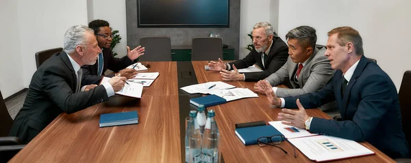 Discussão quente. Empresários multiculturais em trajes formais discutindo algo ao ter uma reunião com parceiros no escritório moderno — Fotografia de Stock