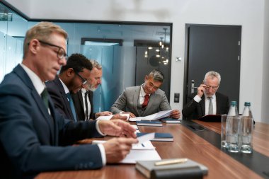 Busy day. Concentrated business people in formal wear reading some documents while having a meeting in the modern office