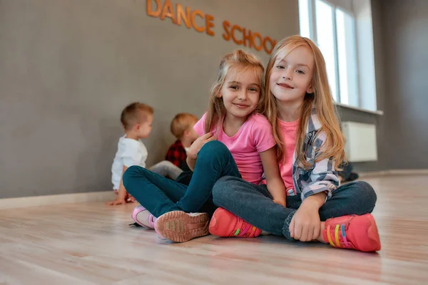 Best friends. Portrait of two happy and cute little girls in casual clothes hugging and smiling at camera while sitting on the floor in the dance studio. Active lifestyle. Choreography concept — 스톡 사진