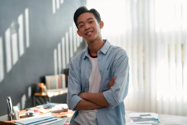 Grande dia de trabalho. Retrato de um jovem asiático alegre em desgaste casual com os braços cruzados olhando para a câmera e sorrindo enquanto estava no escritório moderno. Designer de sucesso — Fotografia de Stock