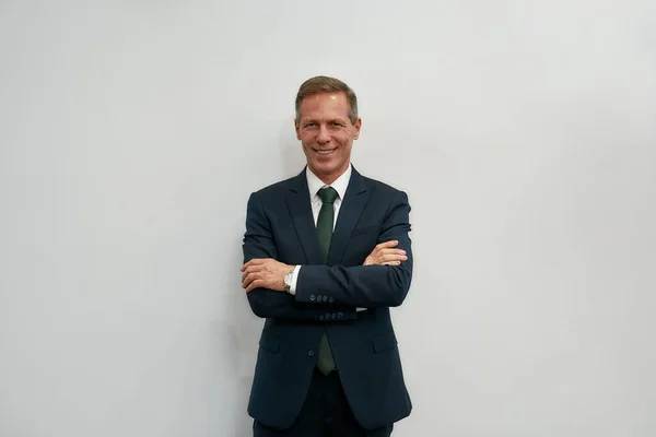 Business expert. Portrait of cheerful mature businessman in classic wear keeping arms crossed and looking at camera while standing against grey background — Stockfoto