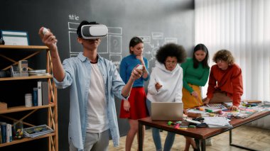 Innovation in business. Young asian man in casual clothes wearing wearing virtual reality headset while his colleagues working on a new project behind him. Web design concept. High Tech