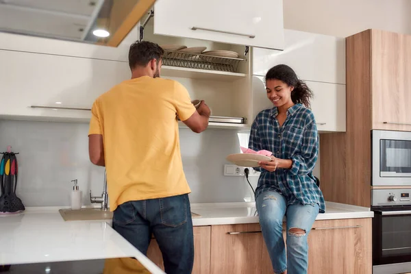 Una casa pulita è una casa felice. Felice coppia multiculturale in abiti casual pulire i piatti e sorridente mentre in piedi nella loro cucina moderna. Pulizia casa — Foto Stock