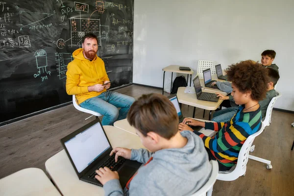 Where Students Are Achievers. Retrato del profesor masculino mirando a la cámara, mientras está sentado con la tableta PC cerca de la pizarra durante una lección en la escuela inteligente moderna. Enfoque selectivo —  Fotos de Stock