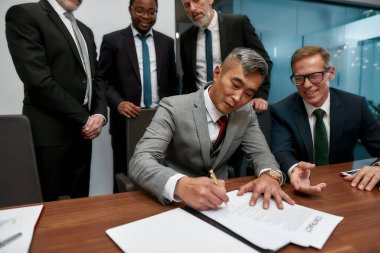 Making a deal. Confident asian businessman signing some document while having a meeting with his business partners in the modern office