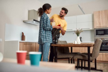 Takım çalışması. Gündelik giysiler içinde genç, çok kültürlü bir çift çöpleri ayırıyor ve modern mutfaklarını temizlerken gülümsüyor.