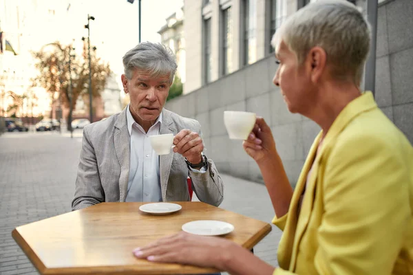 Casal sênior elegante sentado no café ao ar livre e falando sobre algo — Fotografia de Stock