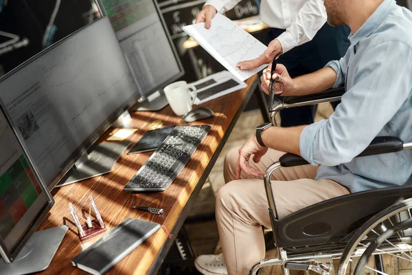 Stock analysis. Cropped photo of male office worker in a wheelchair discussing financial report with his colleague while working together in the office. — ストック写真