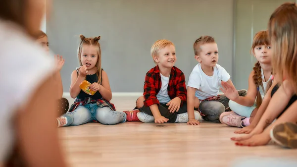 Piccole ballerine. Un gruppo di bambine e ragazzi carini in abiti casual che si parlano mentre si siedono in cerchio durante la lezione di coreografia nello studio di danza — Foto Stock