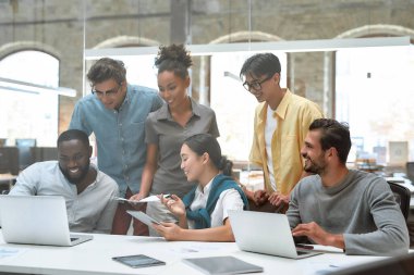 Biz gelmiş geçmiş en iyi takımız. Bir grup genç ve neşeli iş adamı, gündelik kıyafetleriyle proje sonuçlarını tartışıyor ve yaratıcı ofiste otururken gülümsüyor.