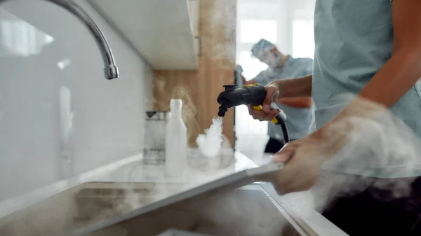 Trabalho sujo. Foto recortada de uma mulher em filtros de limpeza uniformes para capuz de cozinha com aspirador de vapor, enquanto seu colega de trabalho masculino no fundo — Fotografia de Stock