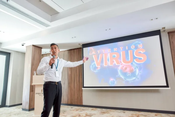 Hör upp. Asiatiska manliga högtalare i kostym med headset och laserpekare hålla ett föredrag på företagens affärsmöte med temat coronavirus — Stockfoto