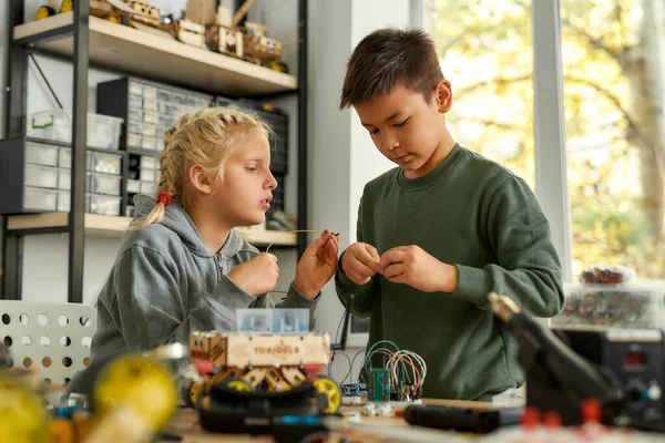 Ideen in die Realität umsetzen. Asiatische Jungen und kaukasische Mädchen bauen ihre eigenen Fahrzeuge in einem Stammrobotikkurs. Erfindungen und Kreativität für Kinder. — Stockfoto