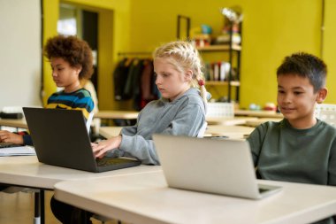 Birlikte herkes daha çok şey başarır. Modern akıllı okul dersleri sırasında diğer öğrencilerle birlikte bilgisayarın ekranına bakan beyaz kız öğrencinin portresi.