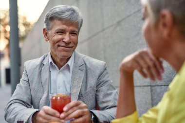 Güzel konuşmaydı. Resmi giyinmiş yakışıklı bir adam elinde kokteyl tutarken ve kafede birlikte otururken gülümseyerek kız arkadaşına bakarken.