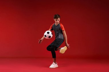 Acele et, vur ve asla pes etme. Sporla meşgul genç bir çocuk, futbol antrenmanı yaparken aşağıya bakıyor. Kırmızı arka planda izole edilmiş. Fitness, eğitim, aktif yaşam tarzı konsepti. Yatay çekim