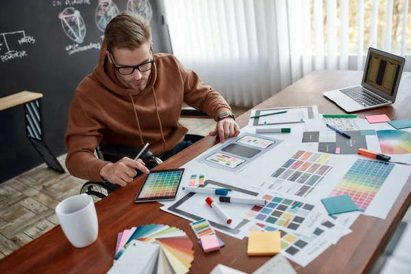 Creatief werker. Geconcentreerde mannelijke ux ontwerper in een rolstoel kiezen van kleurstalen voor mobiele app tijdens het werken op zijn creatieve werkplek in het moderne kantoor — Stockfoto