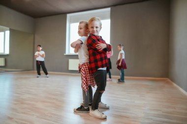 Küçük dansçılar. İki şık çocuk sırt sırta durup dans stüdyosunda dururken gülümseyerek kameraya bakıyorlar. Koreografi sınıfı