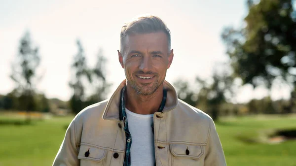 Mooie zonnige dag. Portret van een knappe en stijlvolle man met een baard die naar de camera kijkt en glimlacht terwijl hij midden in het park staat — Stockfoto