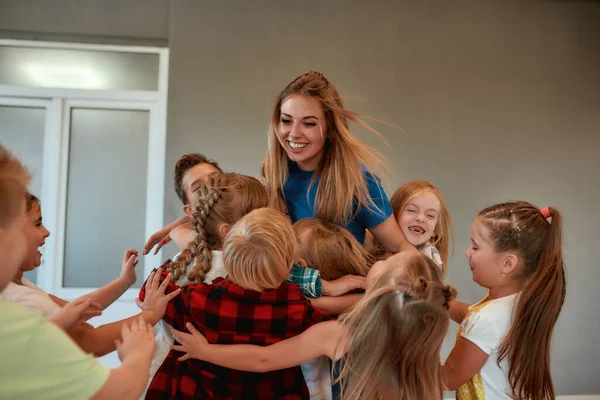 Giovane insegnante di danza femminile positiva che abbraccia bambini felici e sorride in piedi in studio. Rapporto tra insegnante e bambini. Lezione di coreografia — Foto Stock