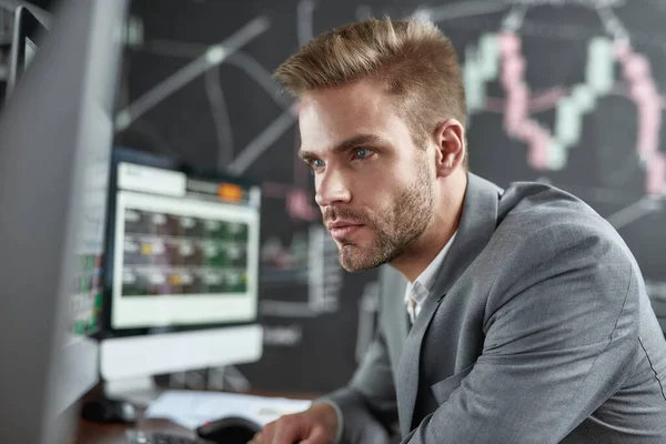 Sueño, estrategia, ganar. Retrato de un joven comerciante exitoso que se ve enfocado mientras está sentado frente a múltiples monitores en la oficina. Pizarra llena de gráficos y análisis de datos en segundo plano . —  Fotos de Stock