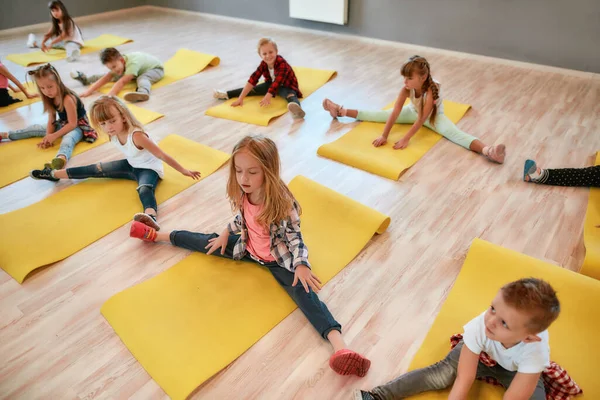 Mi sto scaldando. Gruppo di bambini seduti sul pavimento e che fanno esercizi di ginnastica in studio di danza. Educazione fisica — Foto Stock