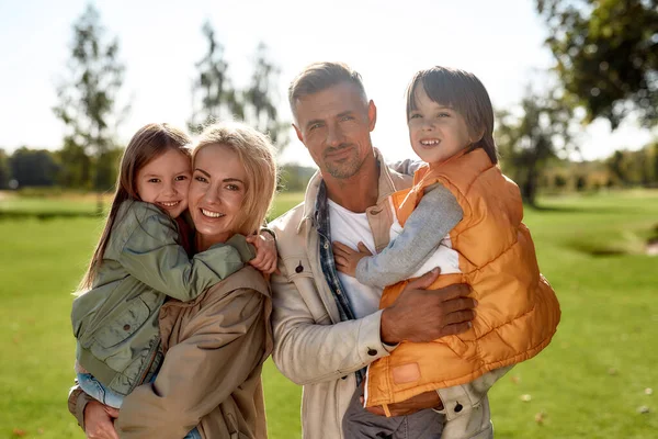 Tillbringa tid tillsammans. Porträtt av glad och vacker familj tittar på kameran med leende när du står i parken på en solig dag — Stockfoto