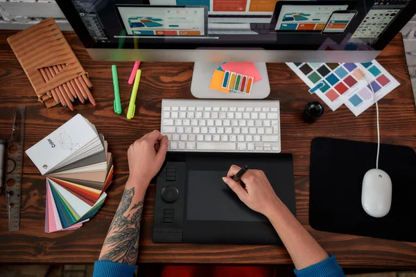 Professional web illustrator. Top view of a graphic designer using graphic tablet and computer in the office or studio. Workplace with graphic tablet, keyboard, computer and color swatches
