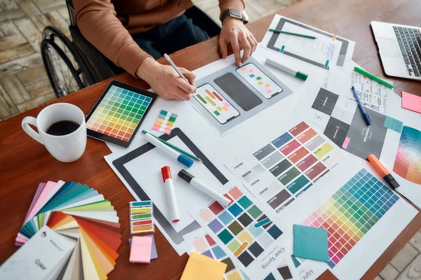 Kullanıcı arayüzü tasarımı. Modern ofisteki yaratıcı işyerinde çalışırken mobil uygulama için doğru renkleri seçen tekerlekli sandalyedeki erkek ux tasarımcısının kesilmiş fotoğrafı.