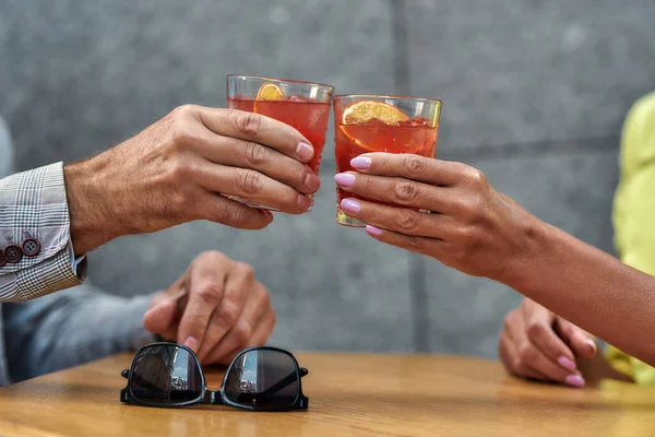 Salud por nosotros. Hombres y mujeres manos sosteniendo cócteles mientras se sienta en la cafetería al aire libre — Foto de Stock