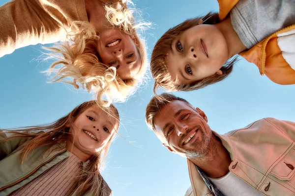 Nuestra familia es la mejor. Vista inferior de la familia feliz y positiva sonriendo a la cámara mientras está de pie al aire libre —  Fotos de Stock