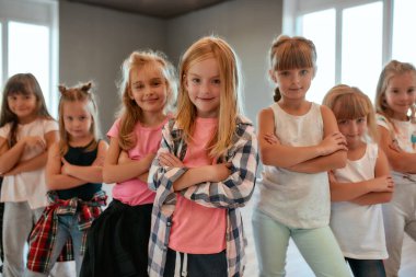 Havalı dansçılar. Dans stüdyosunda dururken kollarını kavuşturup kameraya gülümseyen pozitif küçük kızların portresi. Koreografi sınıfı