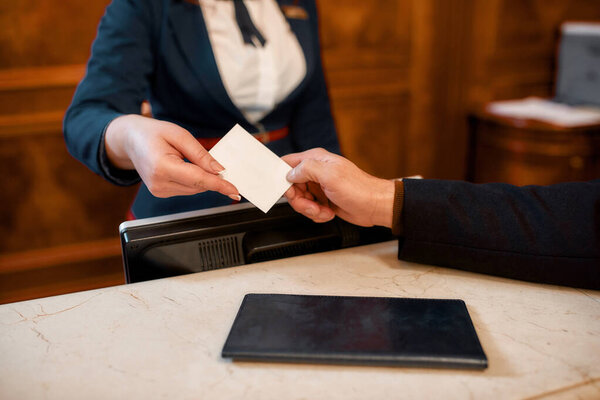 Here is your key. Close up of male and female hands. Smiling female receptionist behind counter in hotel giving key card to the guest.