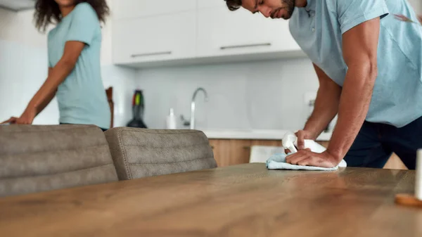 Foto ritagliata di due giovani pulitori professionisti in uniforme che lavorano insieme in cucina. Giovane uomo pulizia tavolo da cucina con strofinare tessile e spray — Foto Stock