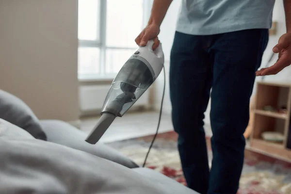 Zugeschnittenes Foto eines Mannes, der Sofa mit Handstaubsauger putzt, während er im Wohnzimmer arbeitet — Stockfoto