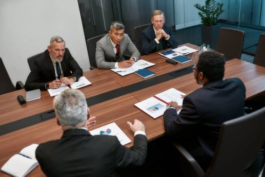 Çok kültürlü iş adamları modern ofiste toplantı yaparken bir şeyler tartışırlar.