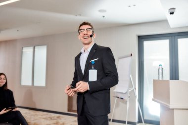Gurur ve Performans. Şirket iş eğitimi konferansında konuşurken gülümseyen kulaklık ve lazer kalemli genç beyaz erkek konuşmacı.