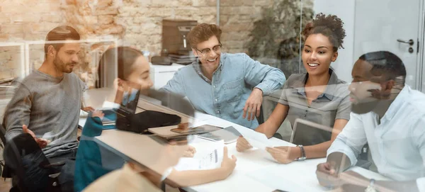 Gemeinsam sind wir mächtig. Gruppe junger Geschäftsleute diskutiert neues Projekt, während sie am Bürotisch hinter der Glaswand im modernen Büro sitzt — Stockfoto
