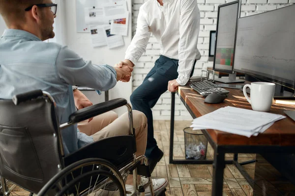 よろしくお願いします。創造的なオフィスで共同作業しながら、彼の同僚に握手車椅子で若い男性オフィスの労働者。障害の概念 — ストック写真