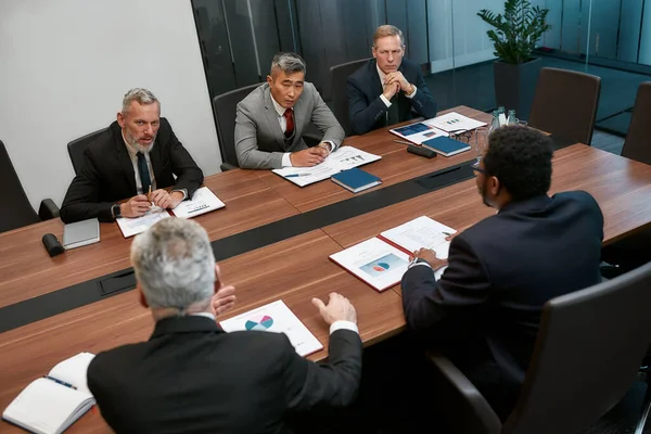 Empresários multiculturais em trajes formais discutindo algo enquanto têm uma reunião no escritório moderno — Fotografia de Stock