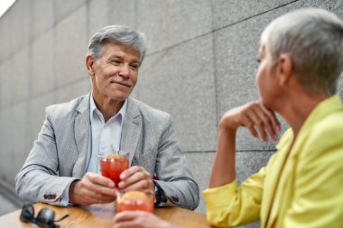 Resmi giyinmiş yakışıklı bir adam elinde kokteyl tutarken ve kafede birlikte otururken gülümseyerek kız arkadaşına bakarken.